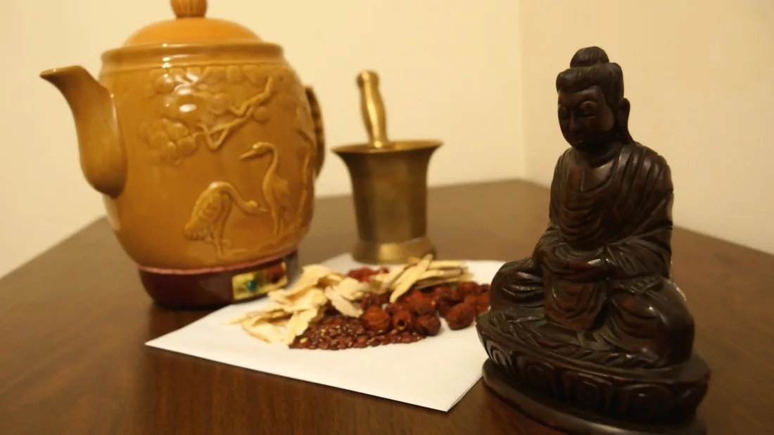 Chinese ceramic teapot, mortar, dried herbs, and a carved figurine arranged on a table